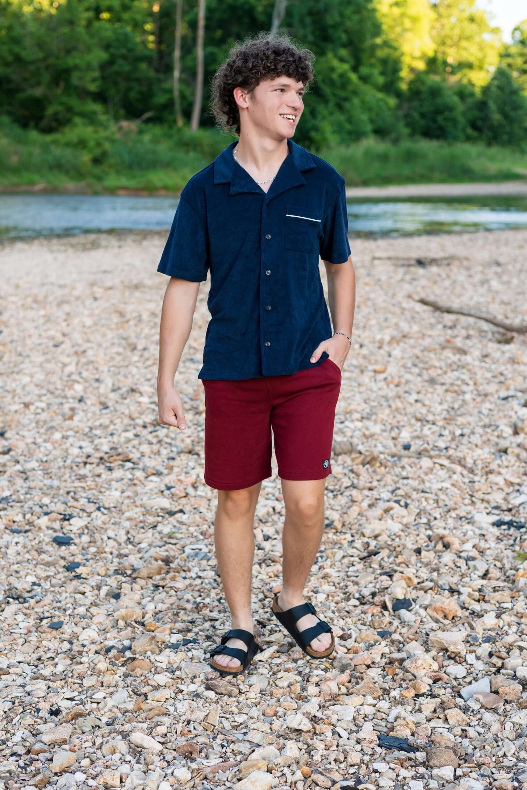 Example Shoot Title Tag A high school senior walks with a hand in his pocket in a blue shirt and smiling over his shoulder away from his Arkansas senior photographer