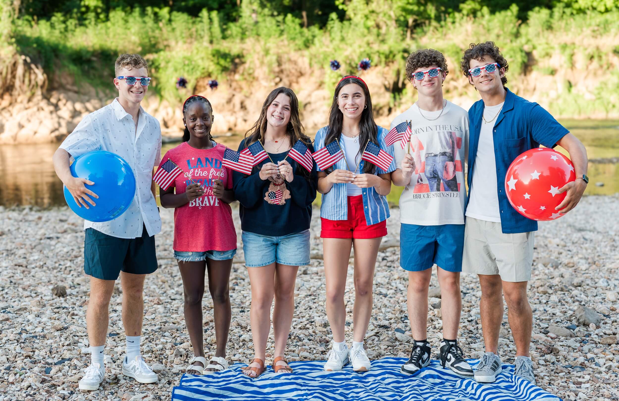 Example Shoot Title Tag Smiling high school seniors stand together celebrating america with flags and glasses by a river