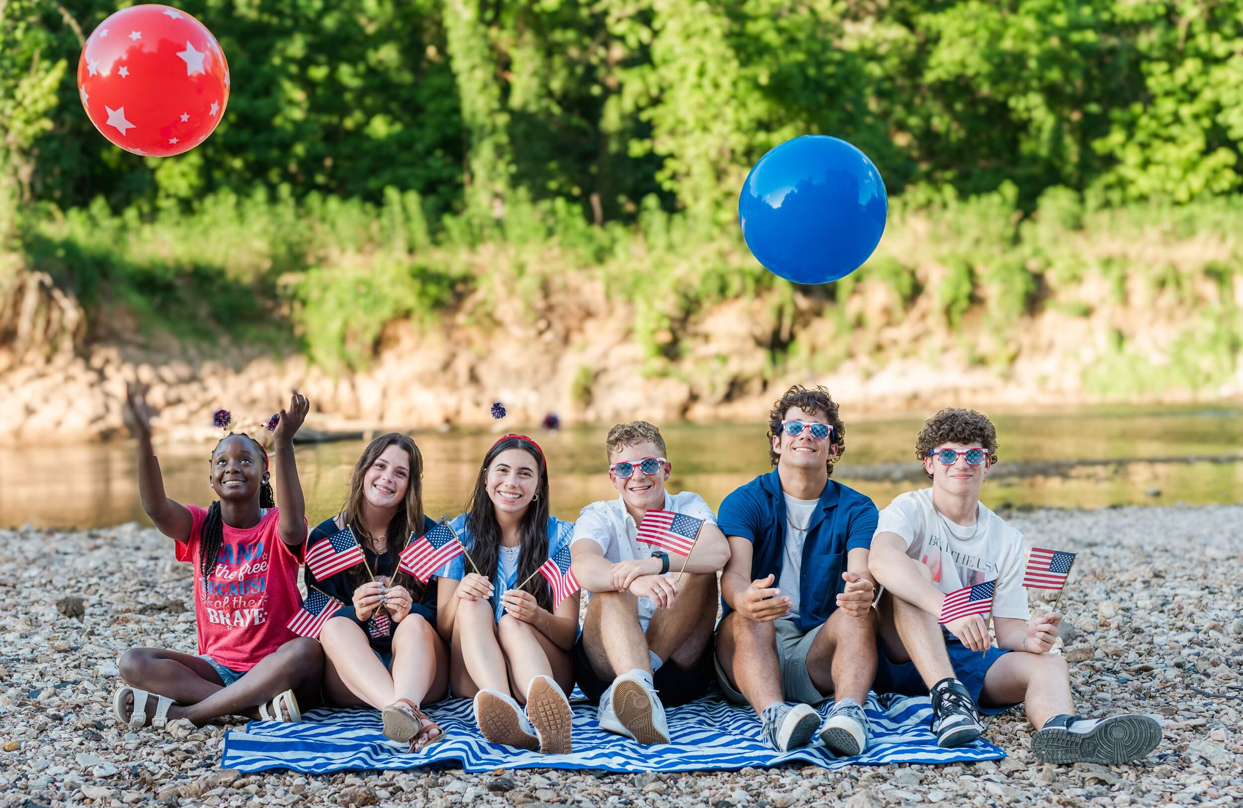 Example Shoot Title Tag Happy high school seniors toss balls in the air while holding american flags and sitting on a beach towel by a river