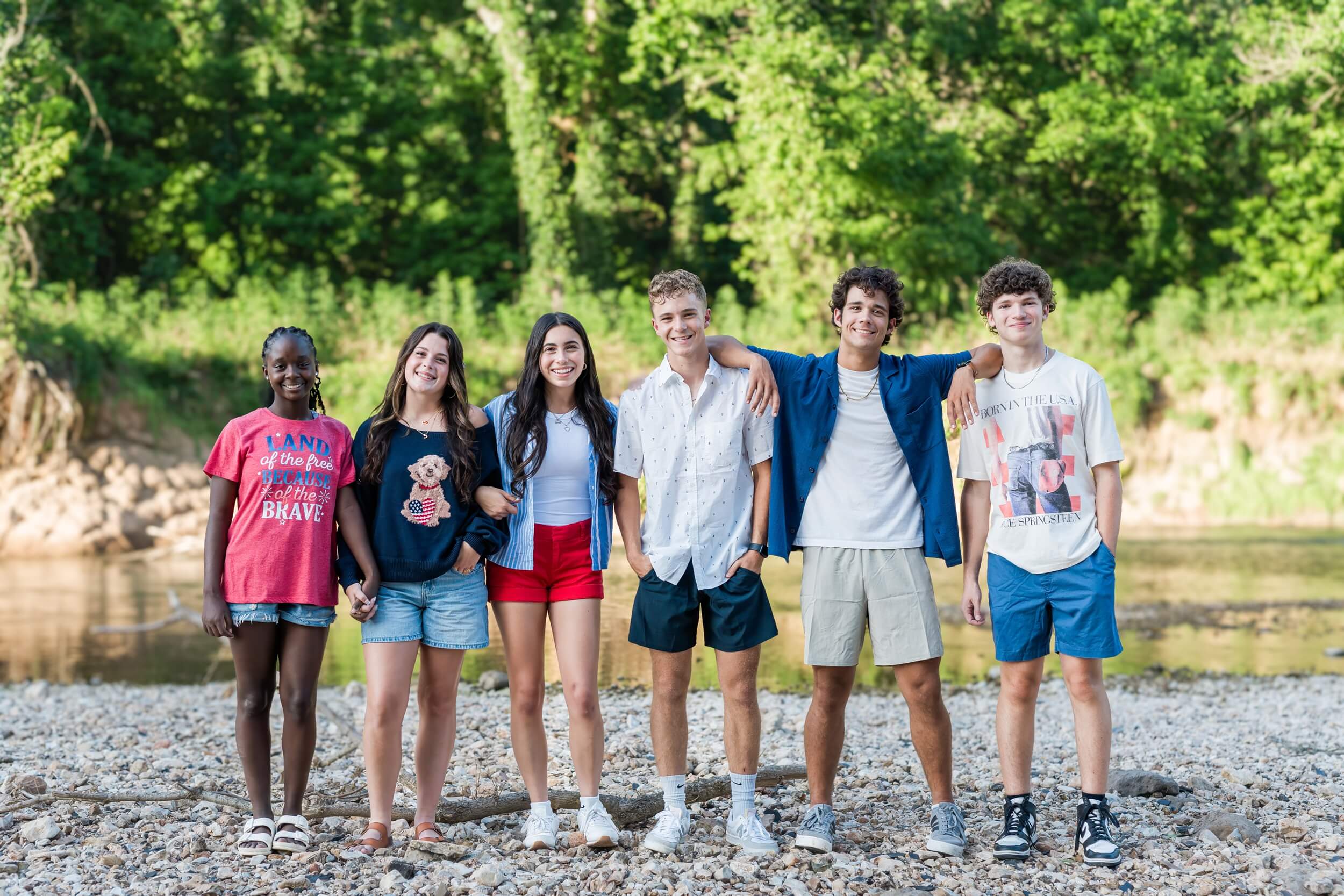 Example Shoot Title Tag A group of six friends hold hands and lean on each other while standing by a river on the rock bed captured by an Arkansas senior photographer