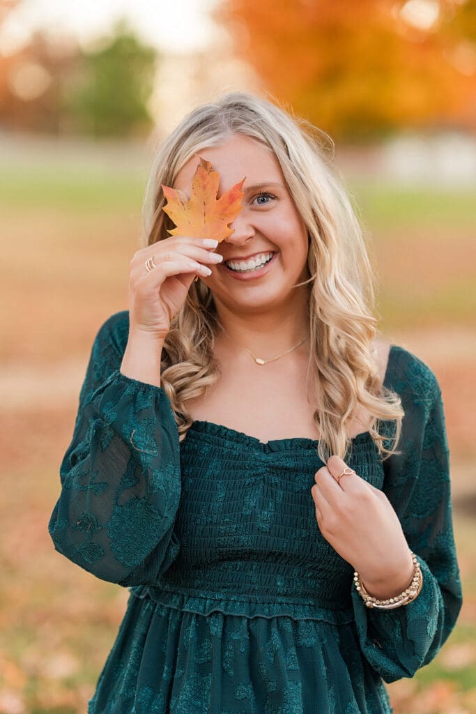 Senior photo in jewel toned dress with fall leaves.