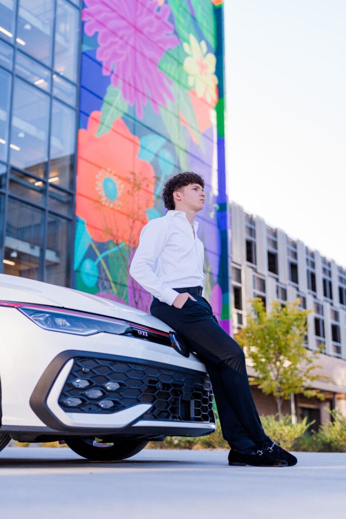 Arkansas senior in suit posing in front of mural with car. 