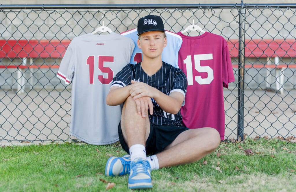 Springdale, Arkansas Senior baseball player sitting in front of Springdale Bulldog jerseys. 