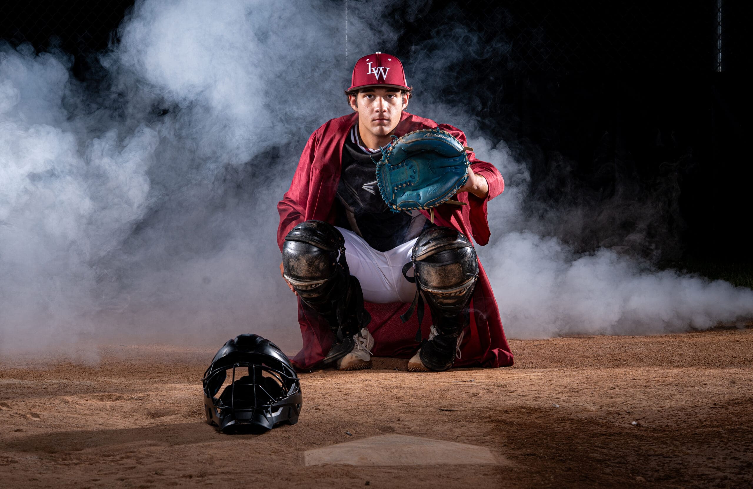 arkansas senior boy playing catcher in cap and gown with smoke behind him.