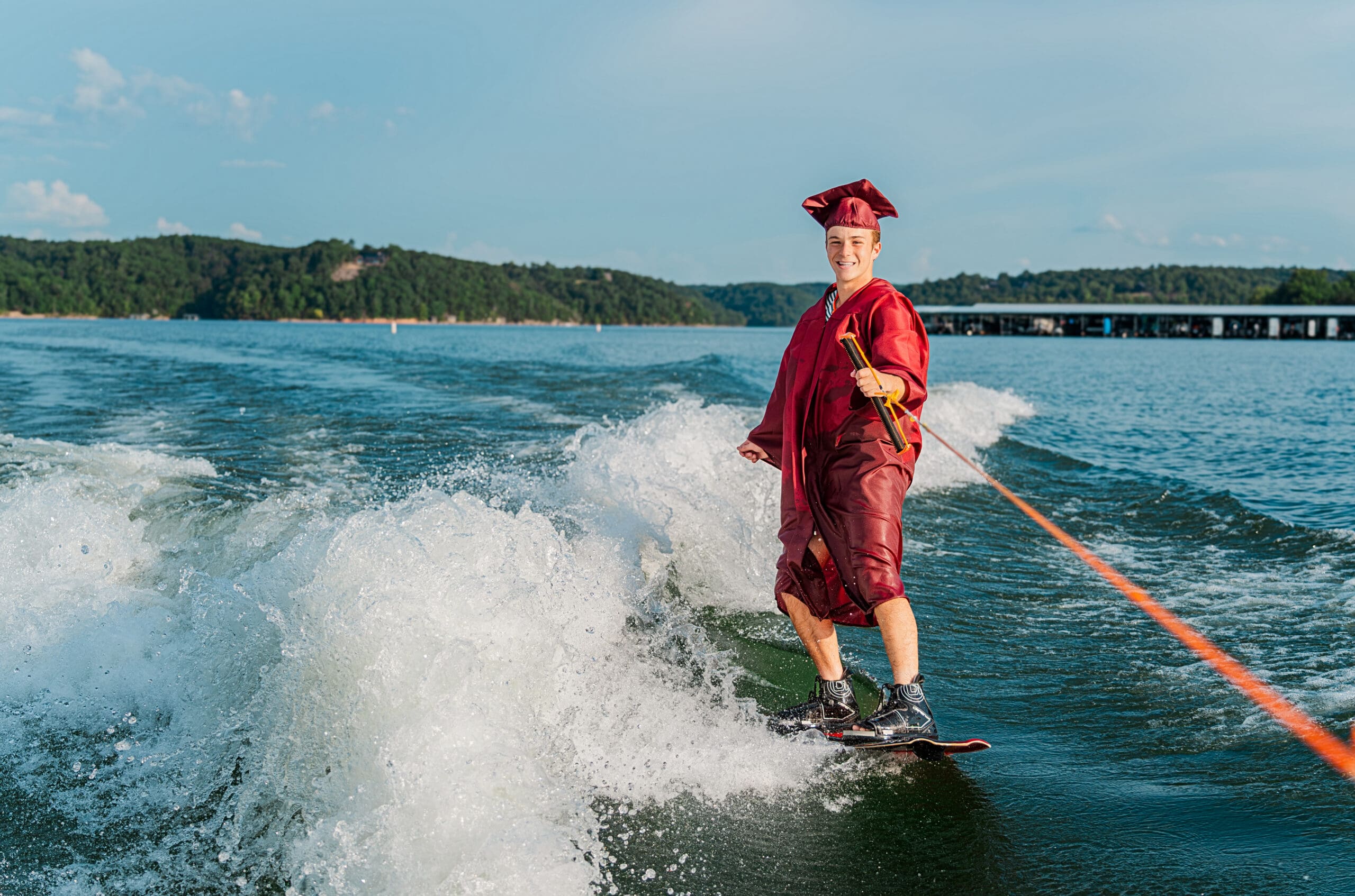 Arkansas senior taking pictures in cap and gown while wake boarding.