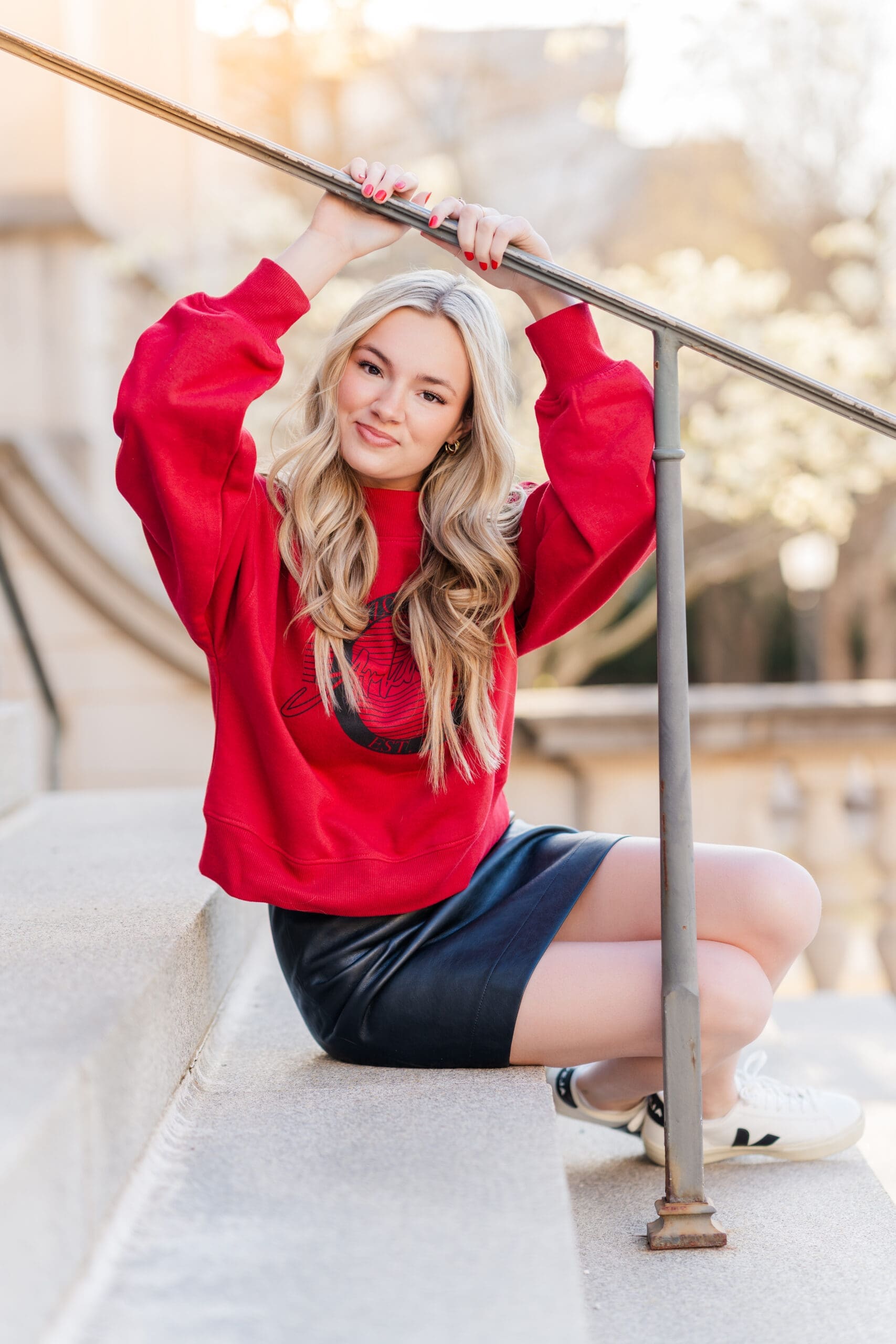 A high school senior sitting on outdoor stone steps in a red graphic sweatshirt and sneakers, photographed by an Arkansas Senior Photographer in a relaxed, natural setting.