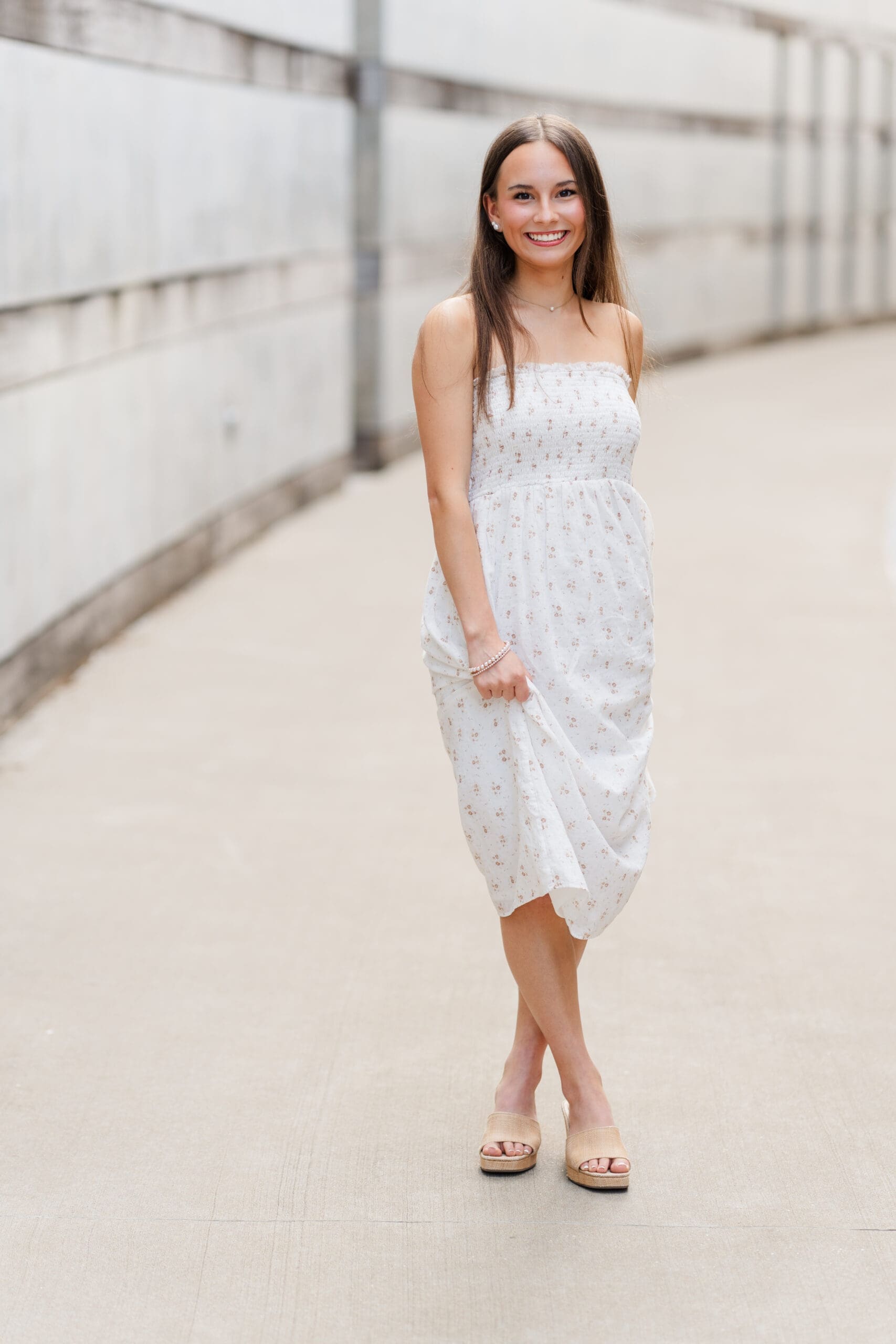 A high school senior in a white strapless dress standing between modern concrete walls, photographed by an Arkansas Senior Photographer in a bright, minimalist outdoor setting.